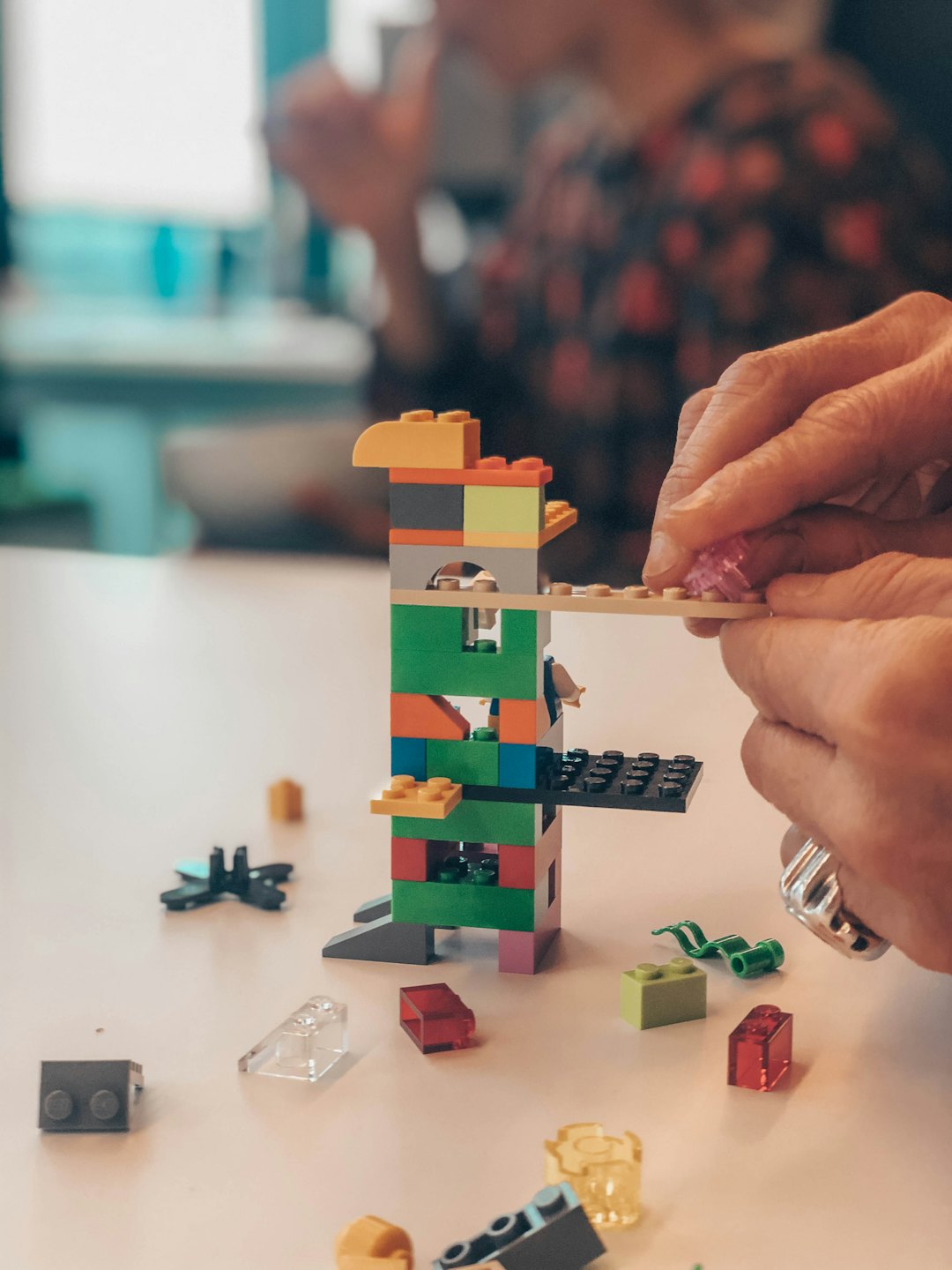Dłonie ostrożnie dodające różowy klocek LEGO do wysokiej wieży.